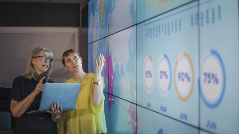 Two woman looking at charts on large wall screen