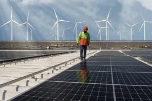 Engineer walking on solar panels with wind turbines in the background