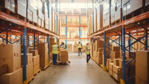 Retail Warehouse full of Shelves with Goods in Cardboard Boxes, Workers Scan and Sort Packages, Move Inventory with Pallet Trucks and Forklifts.