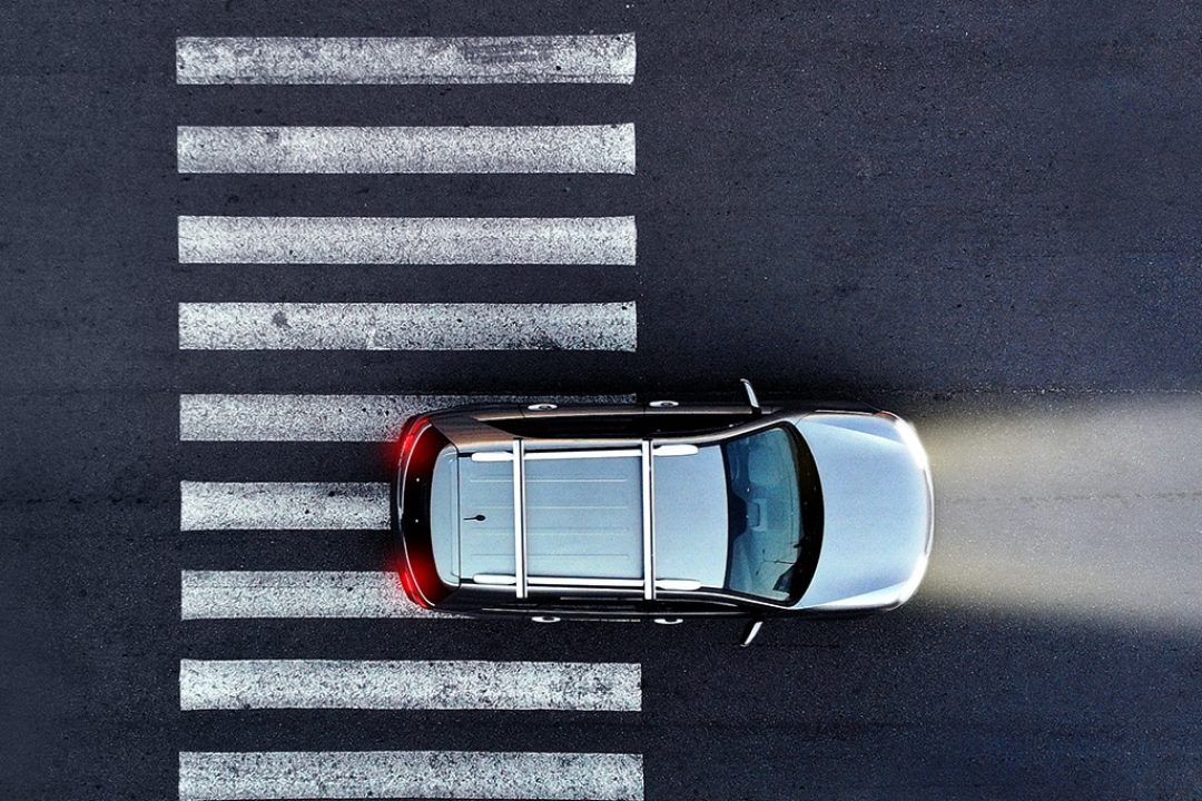 Car with its headlights on drives over a pedestrian crosswalk at night