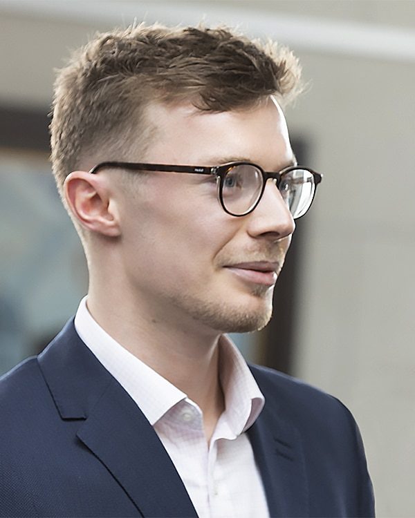 Side view of mid-20s white male with light brown hair and glasses smiling while looking right